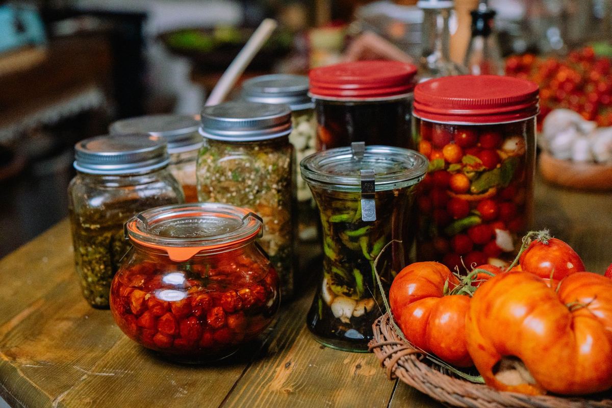 Jars of homemade fermented and preserved vegetables beside fresh tomatoes on a wooden table