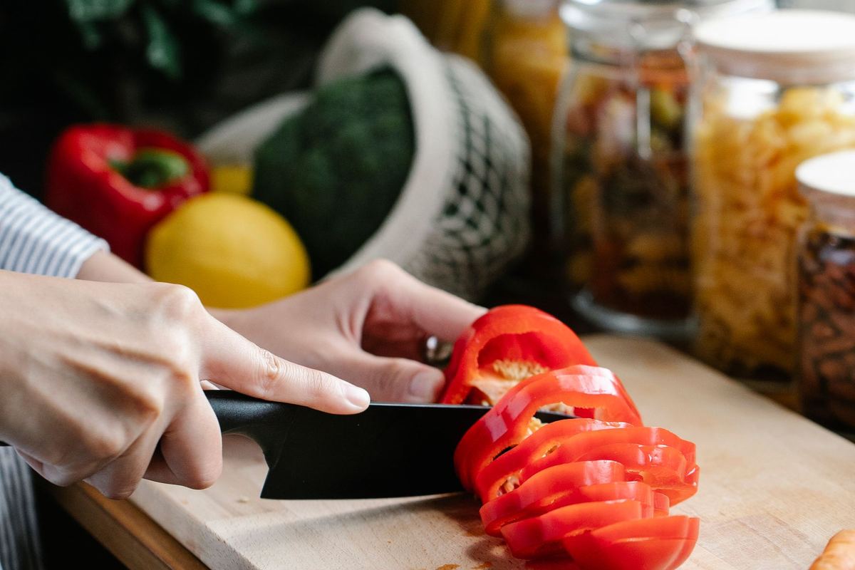 Hands slicing a red bell pepper on a wooden board during meal prep